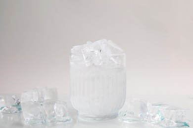 Photo of Refreshing water in glass with ice cubes on light background