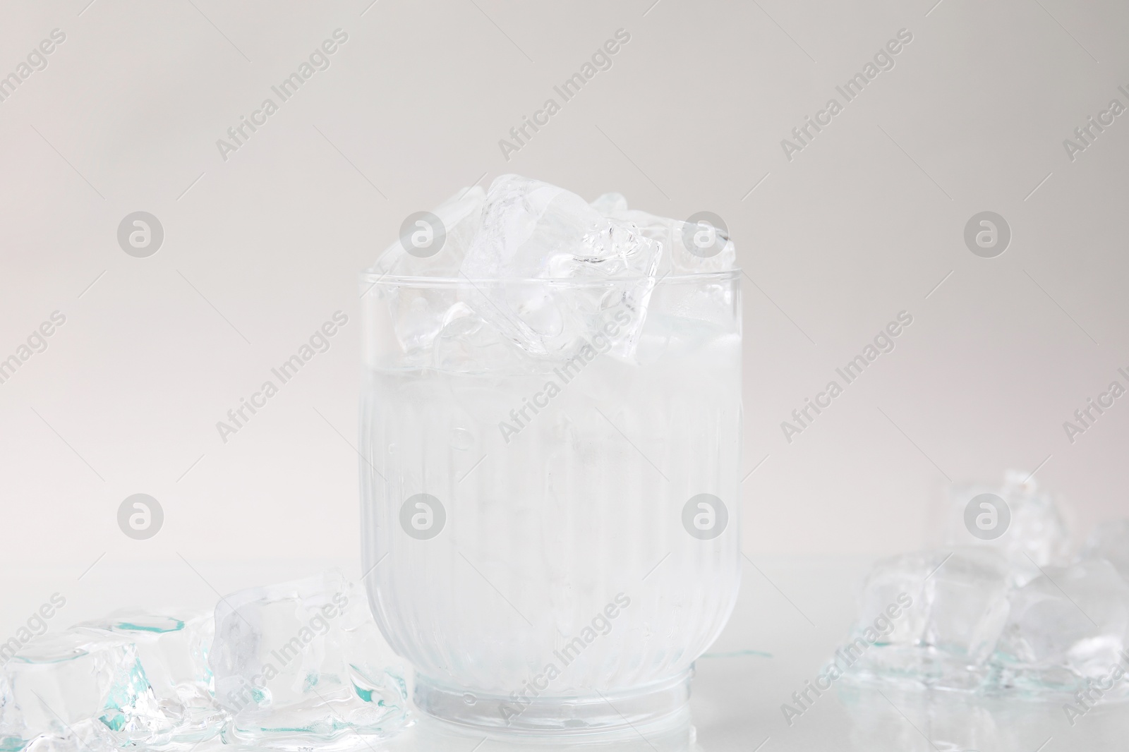 Photo of Refreshing water in glass with ice cubes on light background