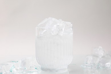 Photo of Refreshing water in glass with ice cubes on light background