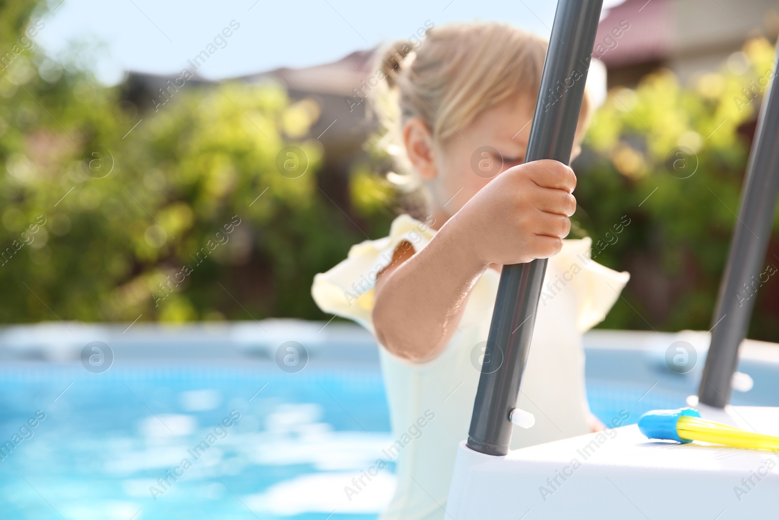 Photo of Little girl getting out of swimming pool by ladder outdoors, selective focus. Space for text