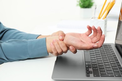 Photo of Carpal tunnel syndrome. Woman suffering from pain in wrist at desk indoors, closeup