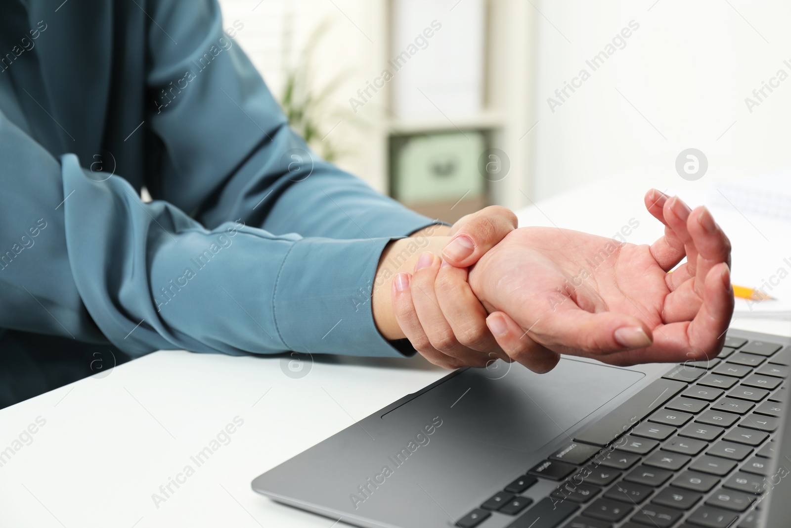 Photo of Carpal tunnel syndrome. Woman suffering from pain in wrist at desk indoors, closeup