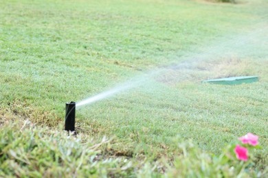 Photo of Automatic sprinkler watering green grass in garden