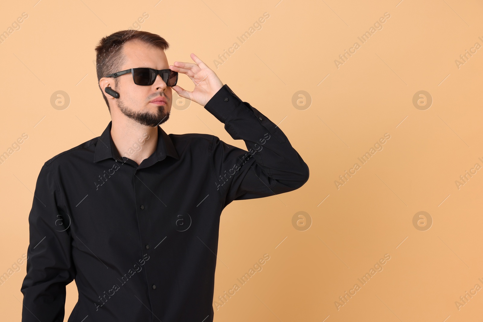 Photo of Young bodyguard in sunglasses and earpiece on beige background, space for text