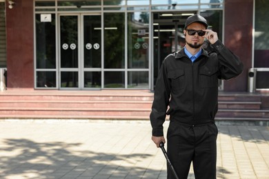 Photo of Security guard in uniform and sunglasses with baton outdoors, space for text