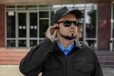 Security guard in uniform and sunglasses using earpiece outdoors