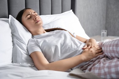 Woman suffering from menstrual pain on bed at home