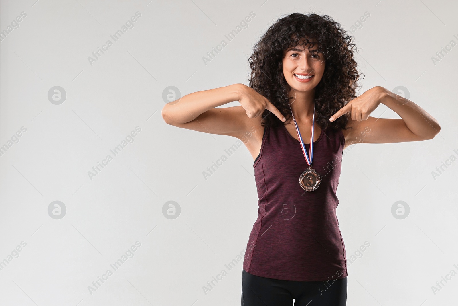 Photo of Happy winner pointing at her bronze medal on light grey background. Space for text