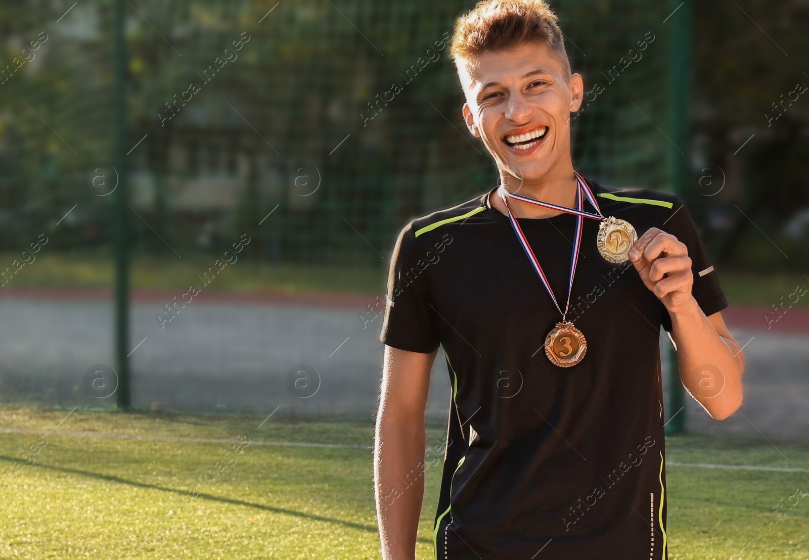 Photo of Happy winner with different medals at stadium. Space for text