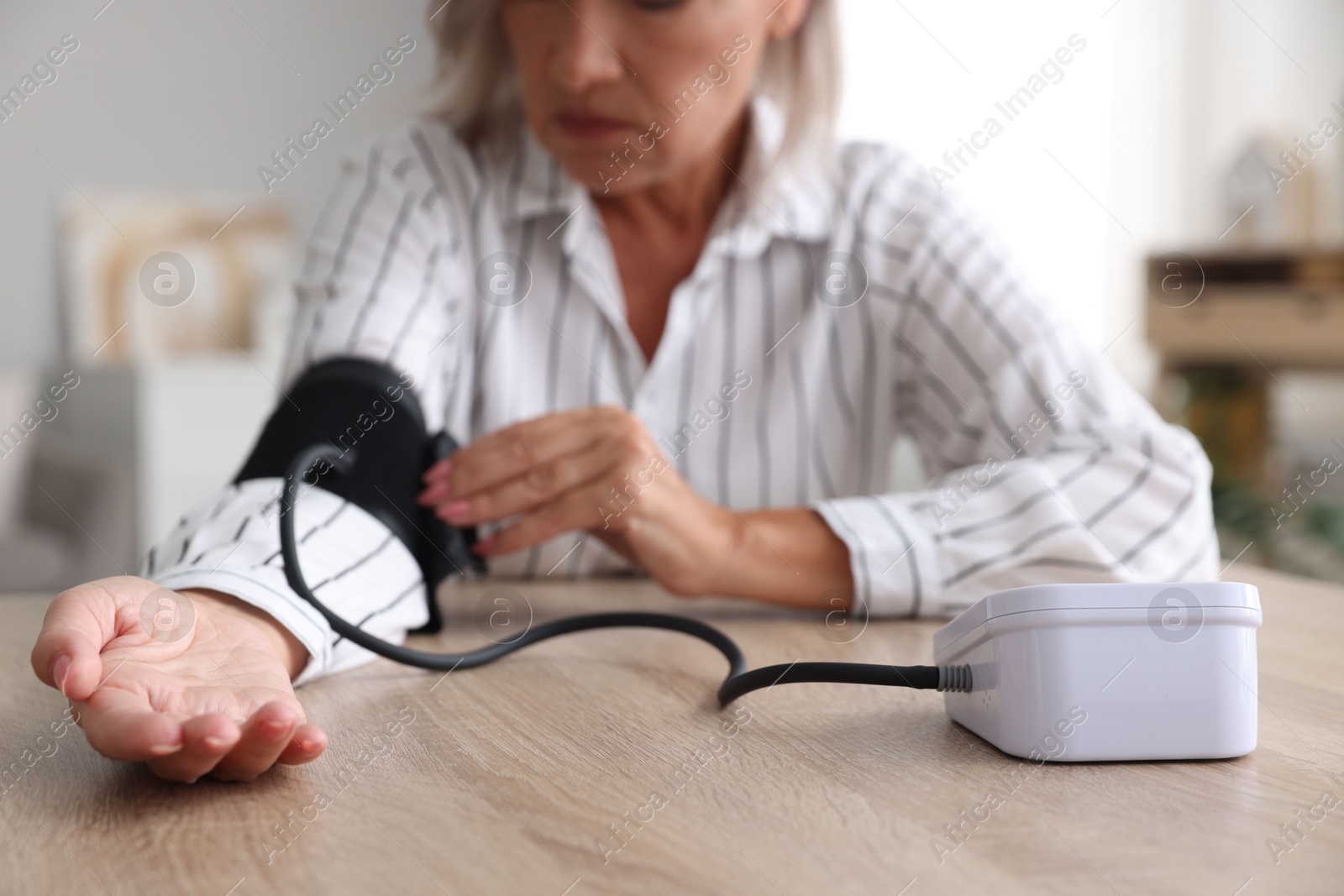 Photo of Woman measuring blood pressure at wooden table indoors, closeup