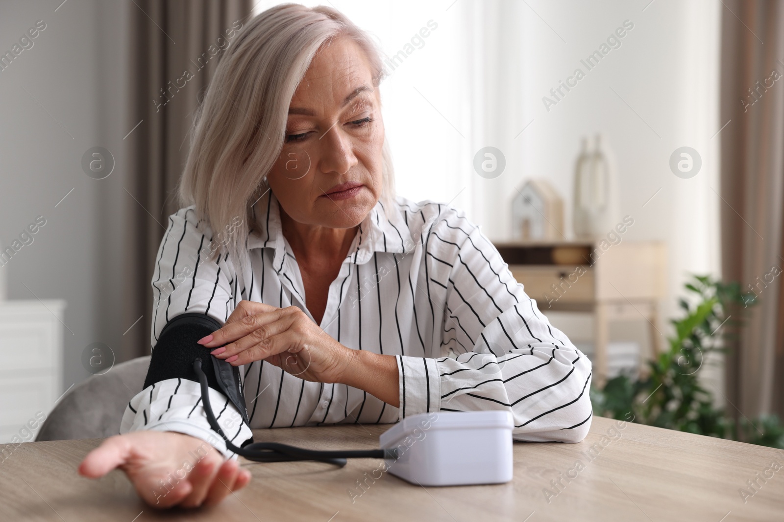 Photo of Woman measuring blood pressure at wooden table indoors