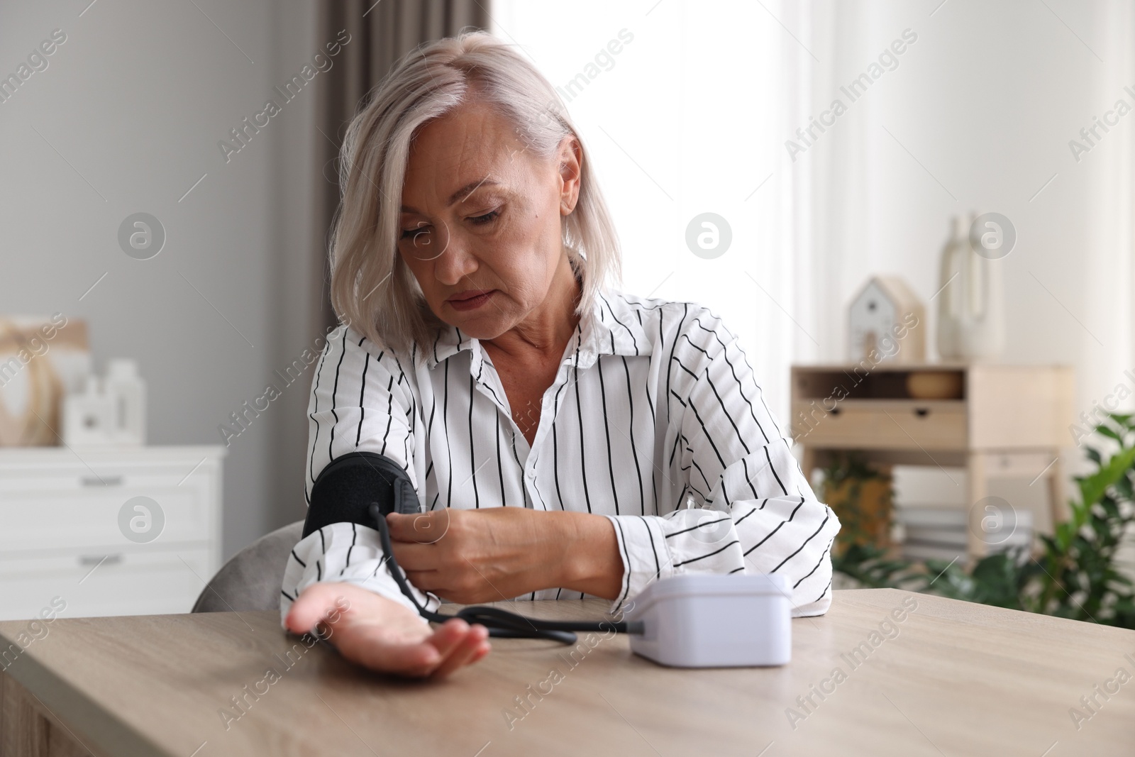 Photo of Woman measuring blood pressure at wooden table indoors