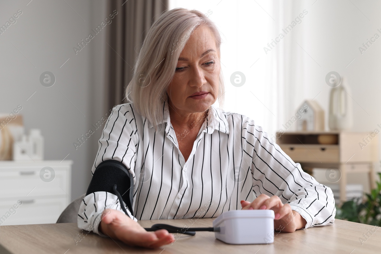 Photo of Woman measuring blood pressure at wooden table indoors