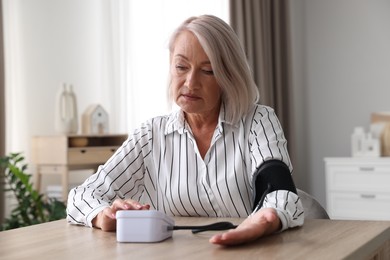 Photo of Woman measuring blood pressure at wooden table indoors