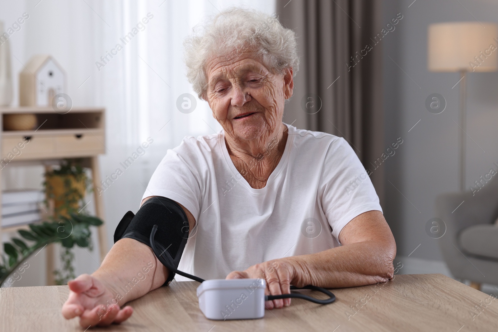 Photo of Senior woman measuring blood pressure at wooden table indoors