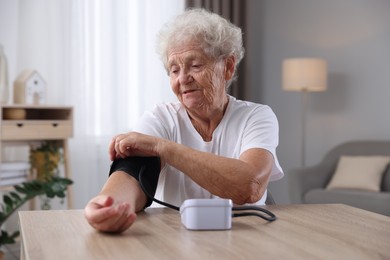 Senior woman measuring blood pressure at wooden table indoors