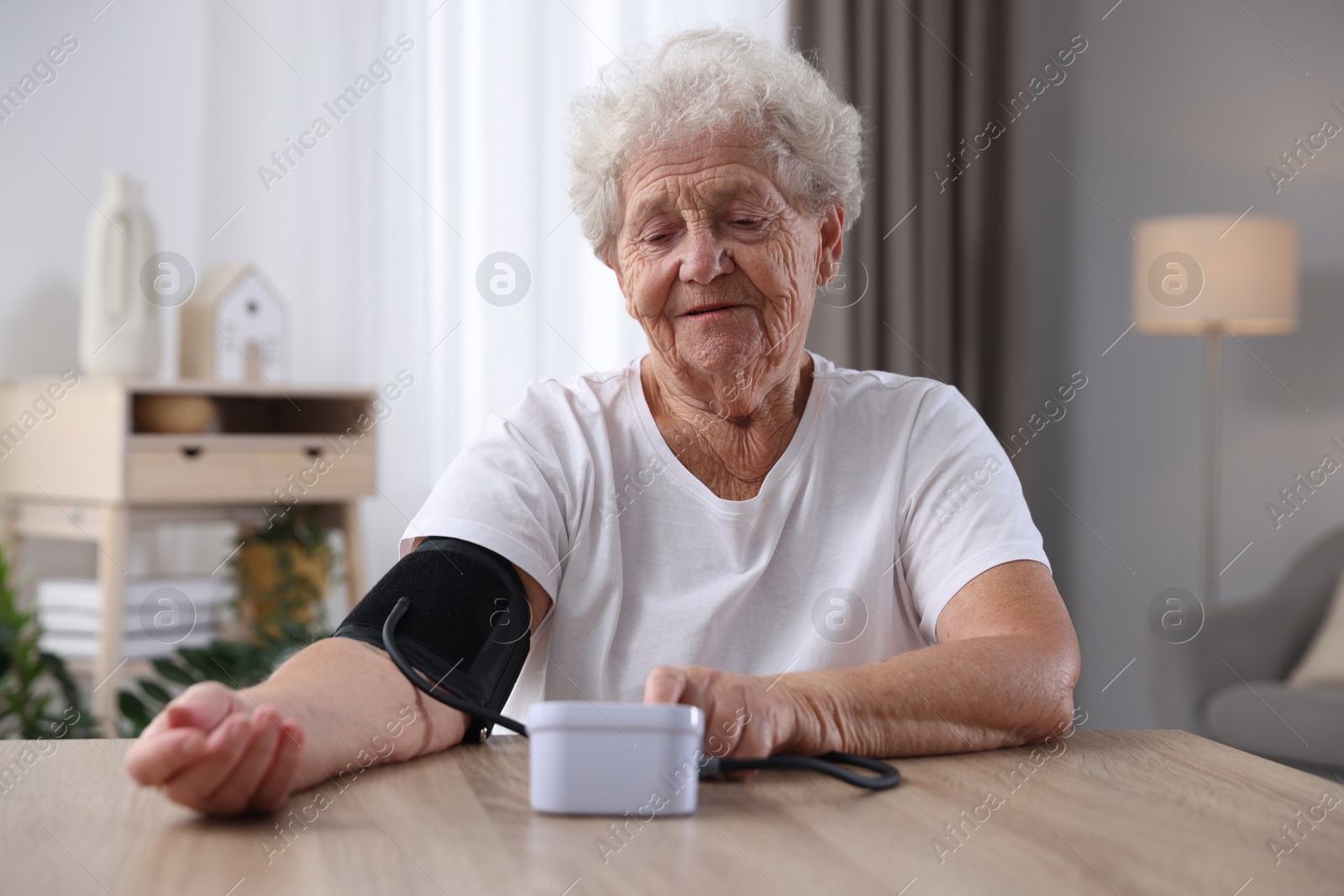 Photo of Senior woman measuring blood pressure at wooden table indoors