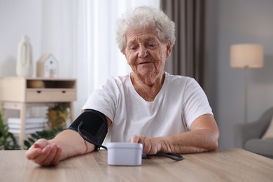 Senior woman measuring blood pressure at wooden table indoors