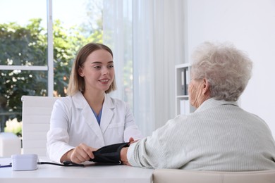 Photo of Doctor measuring patient's blood pressure at table in hospital