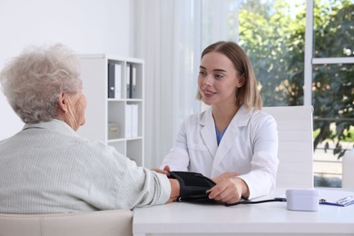 Photo of Doctor measuring patient's blood pressure at table in hospital