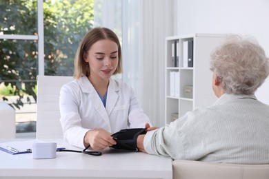 Photo of Doctor measuring patient's blood pressure at table in hospital