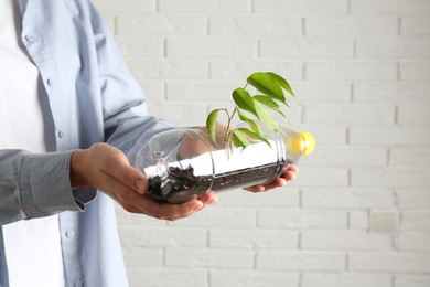 Photo of Recycling concept. Woman holding plastic bottle with growing plant against white brick wall, closeup