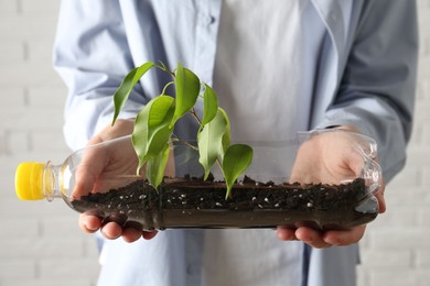 Photo of Recycling concept. Woman holding plastic bottle with growing plant against white background, closeup