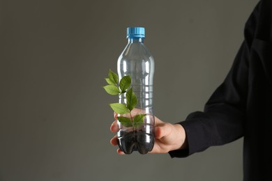 Photo of Recycling concept. Woman holding plastic bottle with growing plant against grey background, closeup