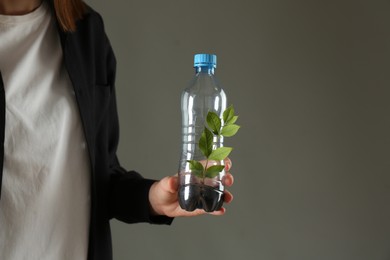 Photo of Recycling concept. Woman holding plastic bottle with growing plant against grey background, closeup. Space for text