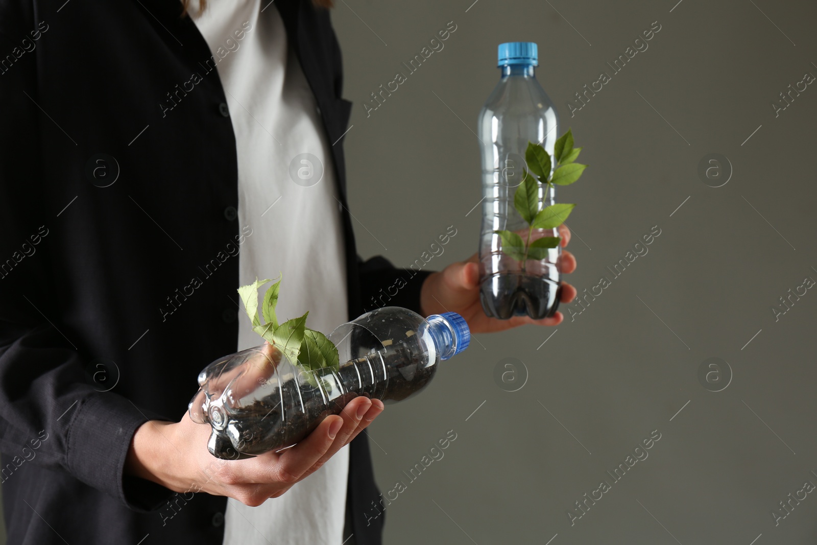 Photo of Recycling concept. Woman holding plastic bottles with growing plants against grey background, closeup