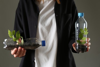 Photo of Recycling concept. Woman holding plastic bottles with growing plants against grey background, closeup