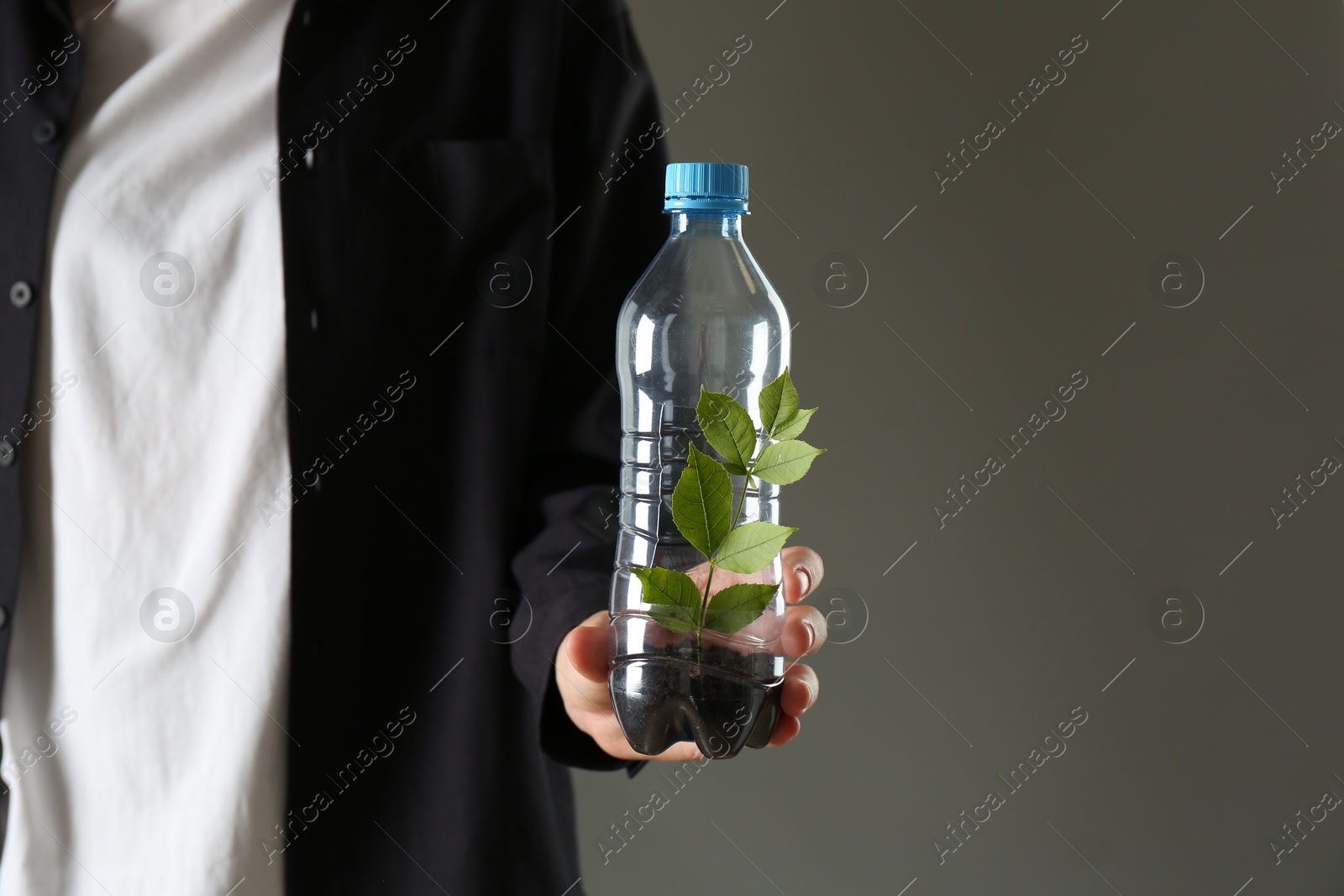 Photo of Recycling concept. Woman holding plastic bottle with growing plant against grey background, closeup. Space for text