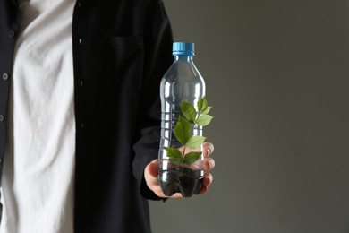 Photo of Recycling concept. Woman holding plastic bottle with growing plant against grey background, closeup. Space for text