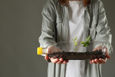 Photo of Recycling concept. Woman holding plastic bottle with growing plant against grey background, closeup. Space for text