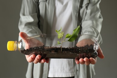 Photo of Recycling concept. Woman holding plastic bottle with growing plant against grey background, closeup