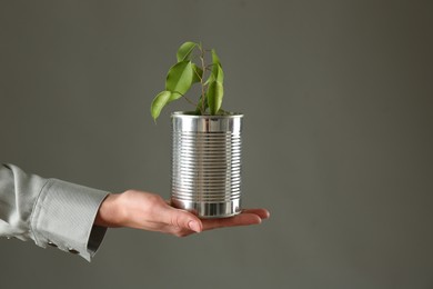 Photo of Recycling concept. Woman holding metal can with growing plant against grey background, closeup. Space for text