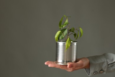 Photo of Recycling concept. Woman holding metal can with growing plant against grey background, closeup. Space for text