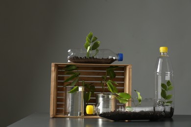 Photo of Recycling concept. Metal cans and plastic bottles with growing plants on grey table