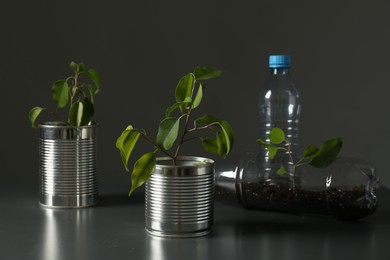 Photo of Recycling concept. Metal cans and plastic bottles with growing plants on grey table