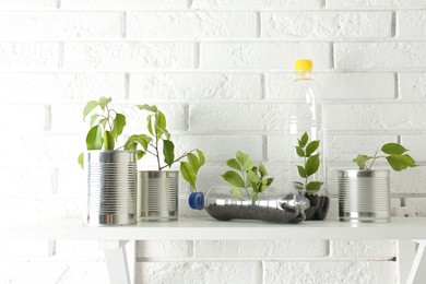 Photo of Recycling concept. Metal cans and plastic bottles with growing plants on white table