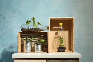 Photo of Recycling concept. Metal cans and plastic bottles with growing plants on side table