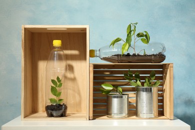 Photo of Recycling concept. Metal cans and plastic bottles with growing plants on white table