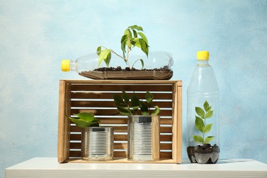 Photo of Recycling concept. Metal cans and plastic bottles with growing plants on white table