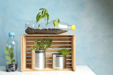 Photo of Recycling concept. Metal cans and plastic bottles with growing plants on white table