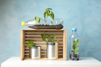 Photo of Recycling concept. Metal cans and plastic bottles with growing plants on white table