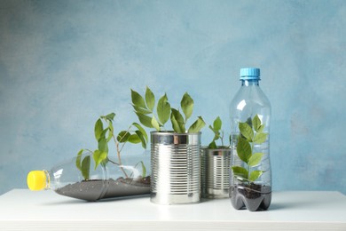 Photo of Recycling concept. Metal cans and plastic bottles with growing plants on white table