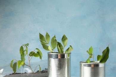 Photo of Recycling concept. Metal cans and plastic bottle with growing plants against light blue background