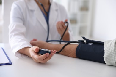 Doctor measuring patient's blood pressure at table in hospital, closeup