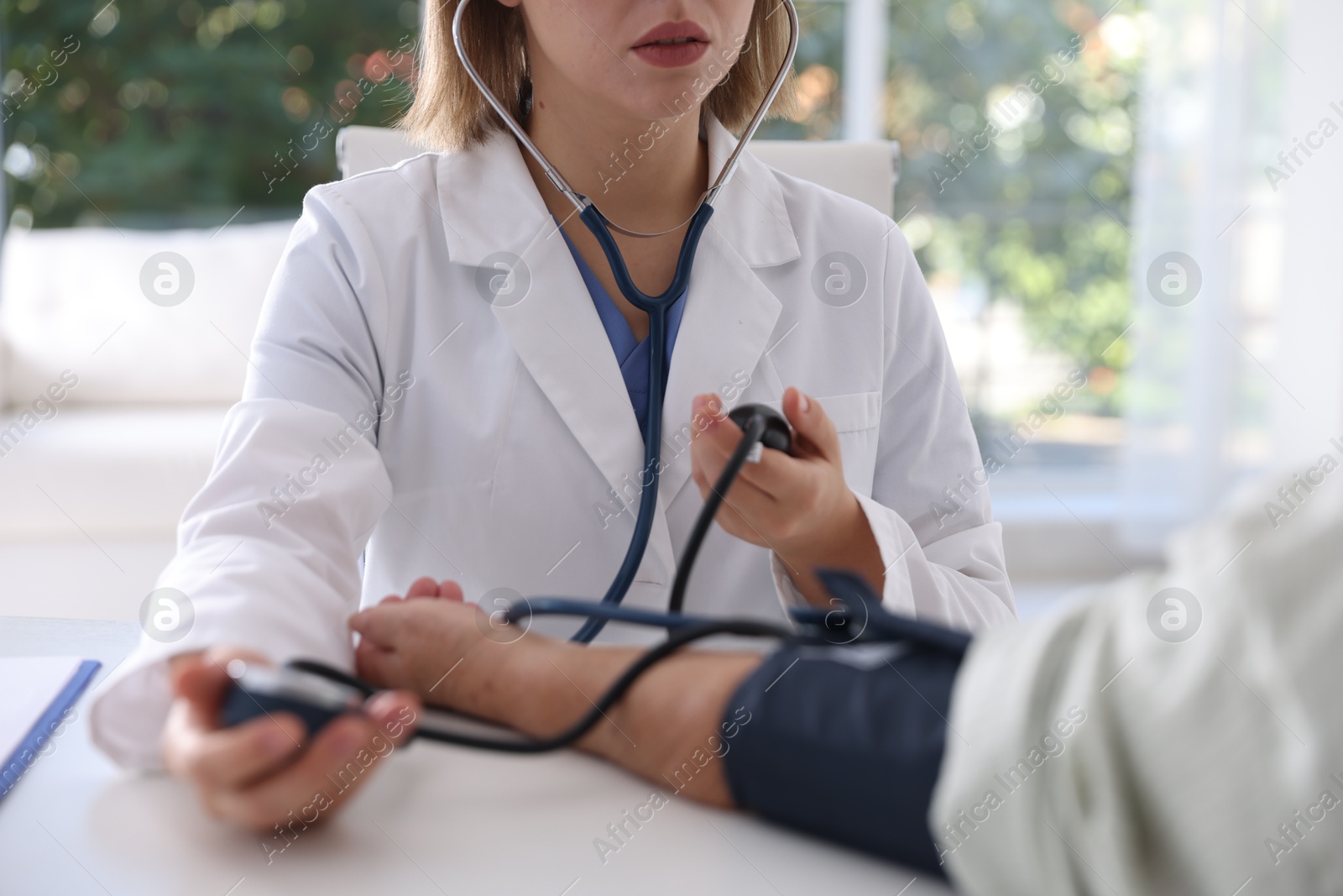 Photo of Doctor measuring patient's blood pressure at table in hospital, closeup