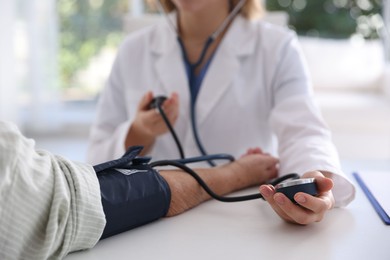 Doctor measuring patient's blood pressure at table in hospital, closeup